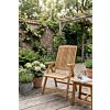 Houten inklapbare tuinstoel en bijzettafel van teak op een vlonder in een sfeervolle tuin met bloemen, een bakstenen muur en een pergola.
