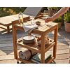 Luxe teakhouten serveerwagen op een zonnig terras, gestyled als buitenbar met wijn en hapjes. Een hand pakt een wijnglas van het bovenblad.