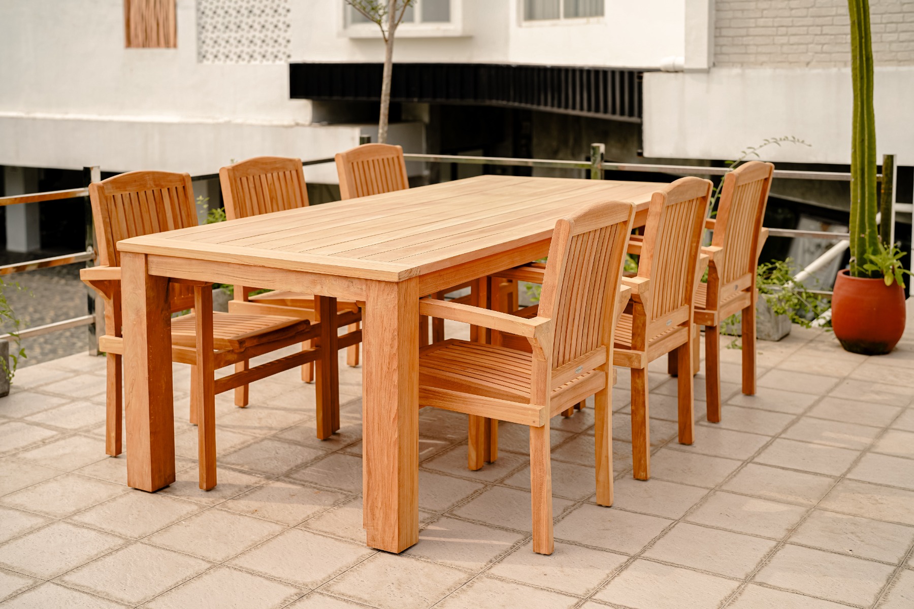 Een sfeervolle foto van een grote, rechthoekige teakhouten tuintafel met zes bijpassende teakhouten stoelen op een zonnig, betegeld terras. De tafel is stijlvol gedekt met linnen lopers, servies, houten schalen met fruit en brood, en kruidenplanten. De st - view 3
